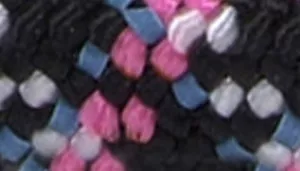 Woven fabric pattern with black strands accented by pink, light blue, and white threads in a diagonal basket-style weave.